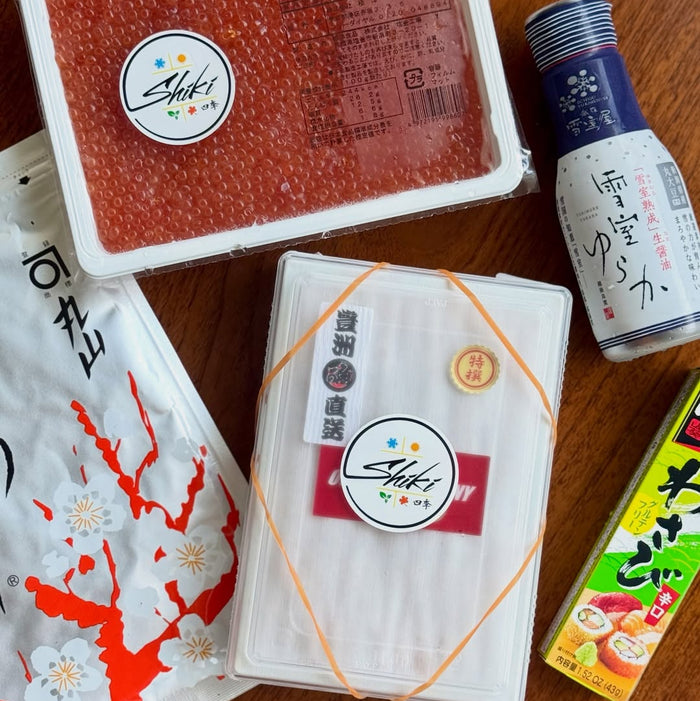 Assorted Japanese products including a box of Sushi, a bottle of Sake, and a package of Wasabi on a wooden surface.